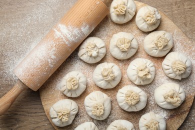 Photo of Uncooked khinkalis (dumplings) and rolling pin on wooden table, top view