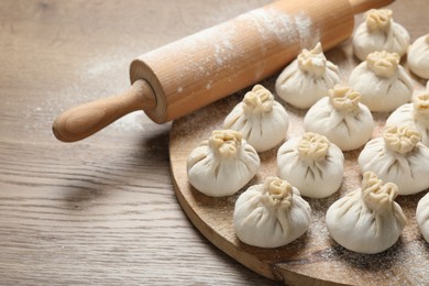 Photo of Uncooked khinkalis (dumplings) and rolling pin on wooden table, closeup