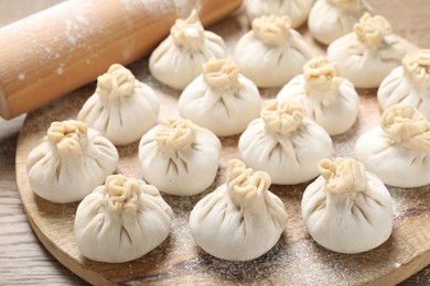 Photo of Uncooked khinkalis (dumplings) and rolling pin on wooden table, closeup