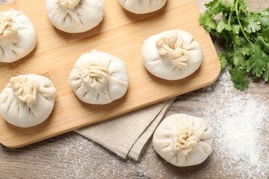 Photo of Uncooked khinkalis (dumplings) and cilantro on wooden table, flat lay