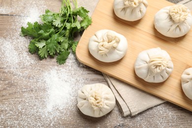 Photo of Uncooked khinkalis (dumplings) and cilantro on wooden table, flat lay