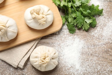 Photo of Uncooked khinkalis (dumplings) and cilantro on wooden table, flat lay. Space for text