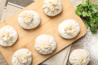 Photo of Uncooked khinkalis (dumplings) and cilantro on wooden table, flat lay