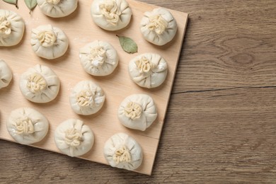 Photo of Uncooked khinkalis (dumplings) and bay leaves on wooden table, top view. Space for text