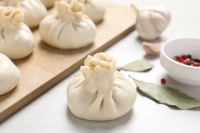 Photo of Uncooked khinkalis (dumplings) and spices on white wooden table, closeup