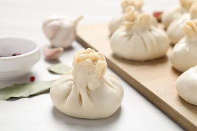 Photo of Uncooked khinkalis (dumplings) and spices on white wooden table, closeup