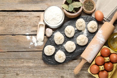 Photo of Uncooked khinkalis (dumplings), flour, spices, eggs and rolling pin on wooden table, flat lay. Space for text