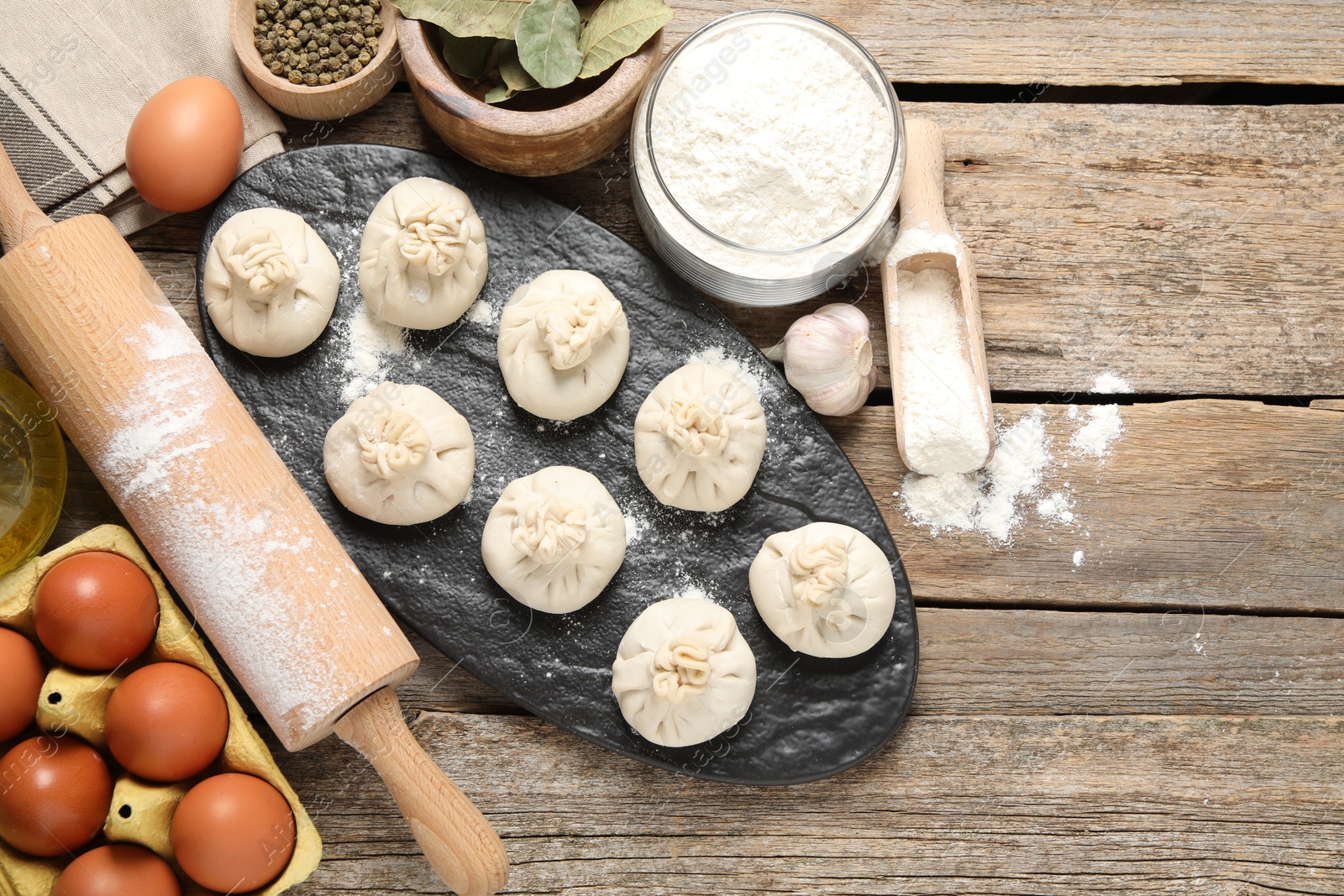 Uncooked khinkalis (dumplings), flour, spices, eggs and rolling pin on wooden table, flat lay. Space for text Photo of Uncooked khinkalis (dumplings), flour, spices, eggs and rolling pin on wooden table, flat lay. Space for text