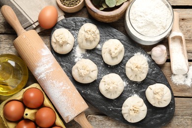 Photo of Uncooked khinkalis (dumplings), flour, spices, eggs and rolling pin on wooden table, flat lay