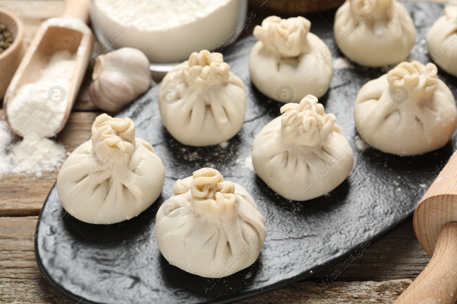 Photo of Uncooked khinkalis (dumplings), flour, garlic and rolling pin on wooden table, closeup
