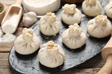 Photo of Uncooked khinkalis (dumplings), flour, garlic and rolling pin on wooden table, closeup