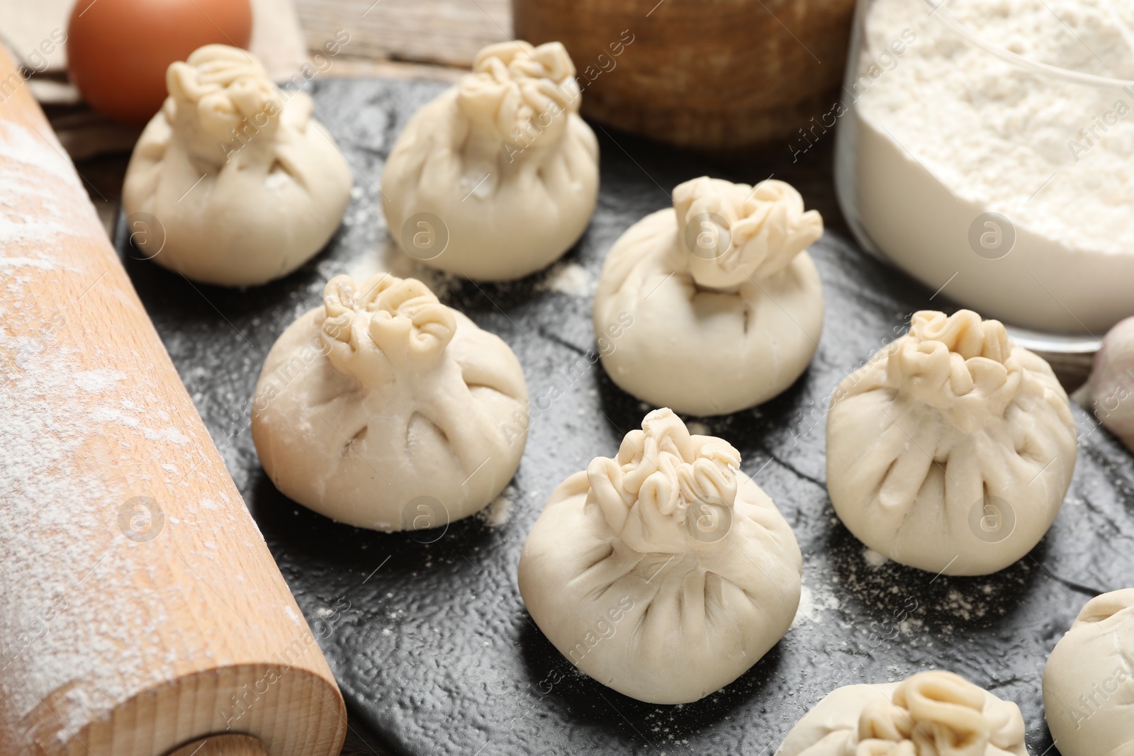 Uncooked khinkalis (dumplings), flour, egg and rolling pin on table, closeup Photo of Uncooked khinkalis (dumplings), flour, egg and rolling pin on table, closeup