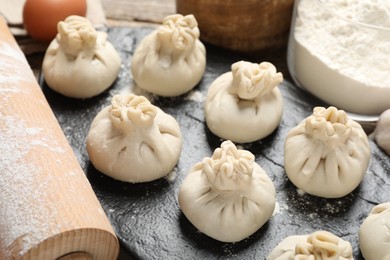 Photo of Uncooked khinkalis (dumplings), flour, egg and rolling pin on table, closeup