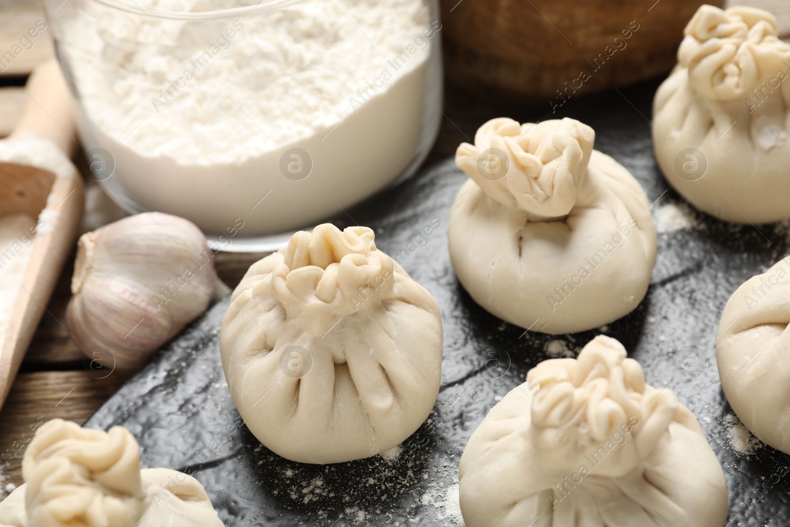 Uncooked khinkalis (dumplings), flour and garlic on table, closeup Photo of Uncooked khinkalis (dumplings), flour and garlic on table, closeup