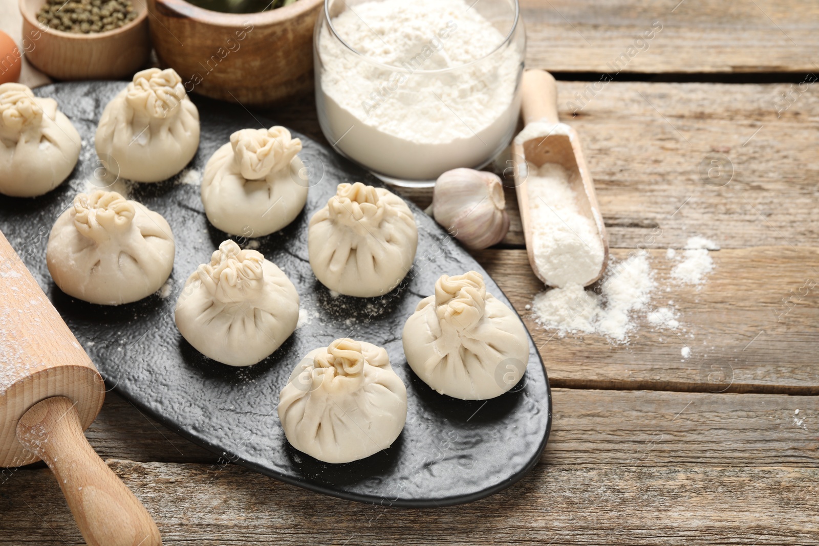Uncooked khinkalis (dumplings), flour, spices and rolling pin on wooden table, closeup. Space for text Photo of Uncooked khinkalis (dumplings), flour, spices and rolling pin on wooden table, closeup. Space for text