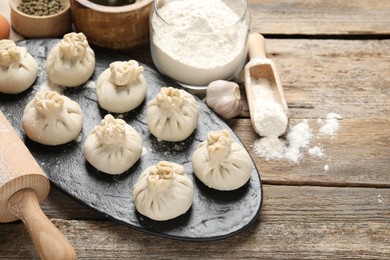 Photo of Uncooked khinkalis (dumplings), flour, spices and rolling pin on wooden table, closeup. Space for text