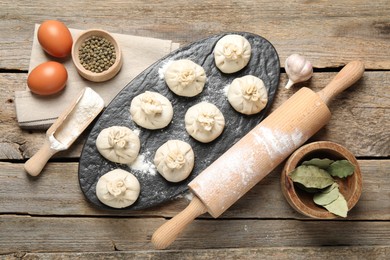 Photo of Uncooked khinkalis (dumplings), flour, spices, eggs and rolling pin on wooden table, flat lay