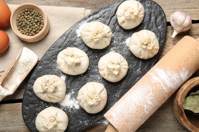 Photo of Uncooked khinkalis (dumplings), flour, spices, eggs and rolling pin on wooden table, flat lay