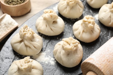 Photo of Uncooked khinkalis (dumplings), flour, spices and rolling pin on table, closeup