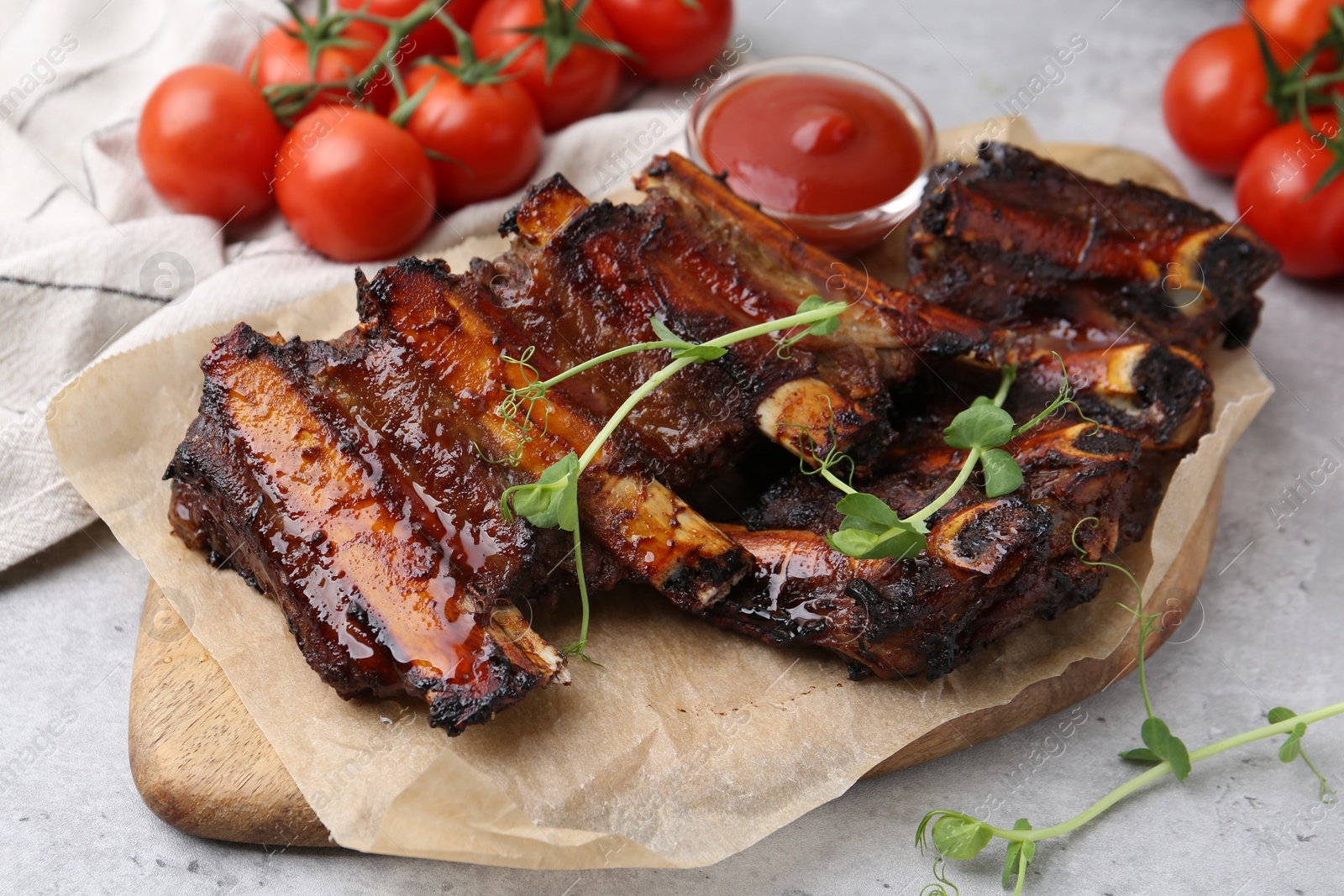 Roasted beef ribs with microgreens, tomatoes and sauce on gray textured table, closeup Photo of Roasted beef ribs with microgreens, tomatoes and sauce on gray textured table, closeup