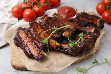 Photo of Roasted beef ribs with microgreens, tomatoes and sauce on gray textured table, closeup