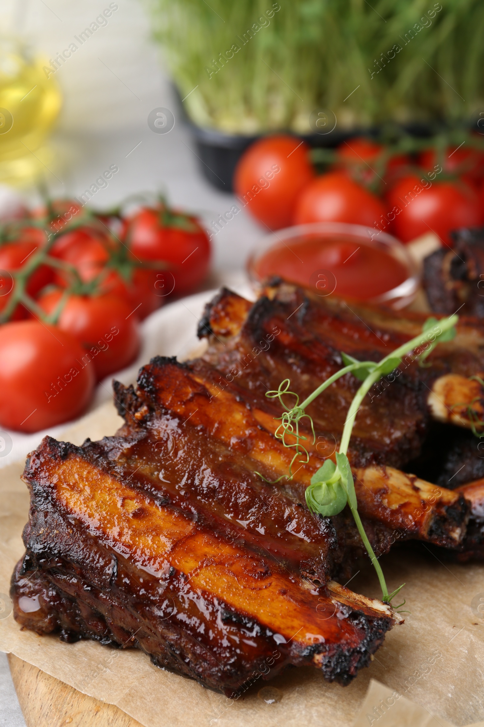 Roasted beef ribs with microgreens, tomatoes and sauce on table, closeup Photo of Roasted beef ribs with microgreens, tomatoes and sauce on table, closeup
