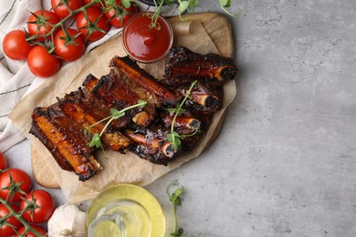 Photo of Roasted beef ribs with microgreens, tomatoes and other products on gray textured table, flat lay. Space for text