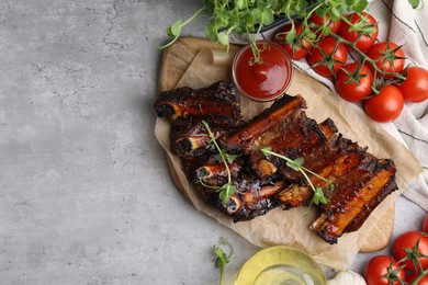 Photo of Roasted beef ribs with microgreens, tomatoes and other products on gray textured table, flat lay. Space for text