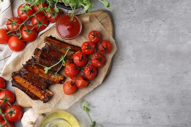 Photo of Roasted beef ribs with microgreens, tomatoes and other products on gray textured table, flat lay. Space for text