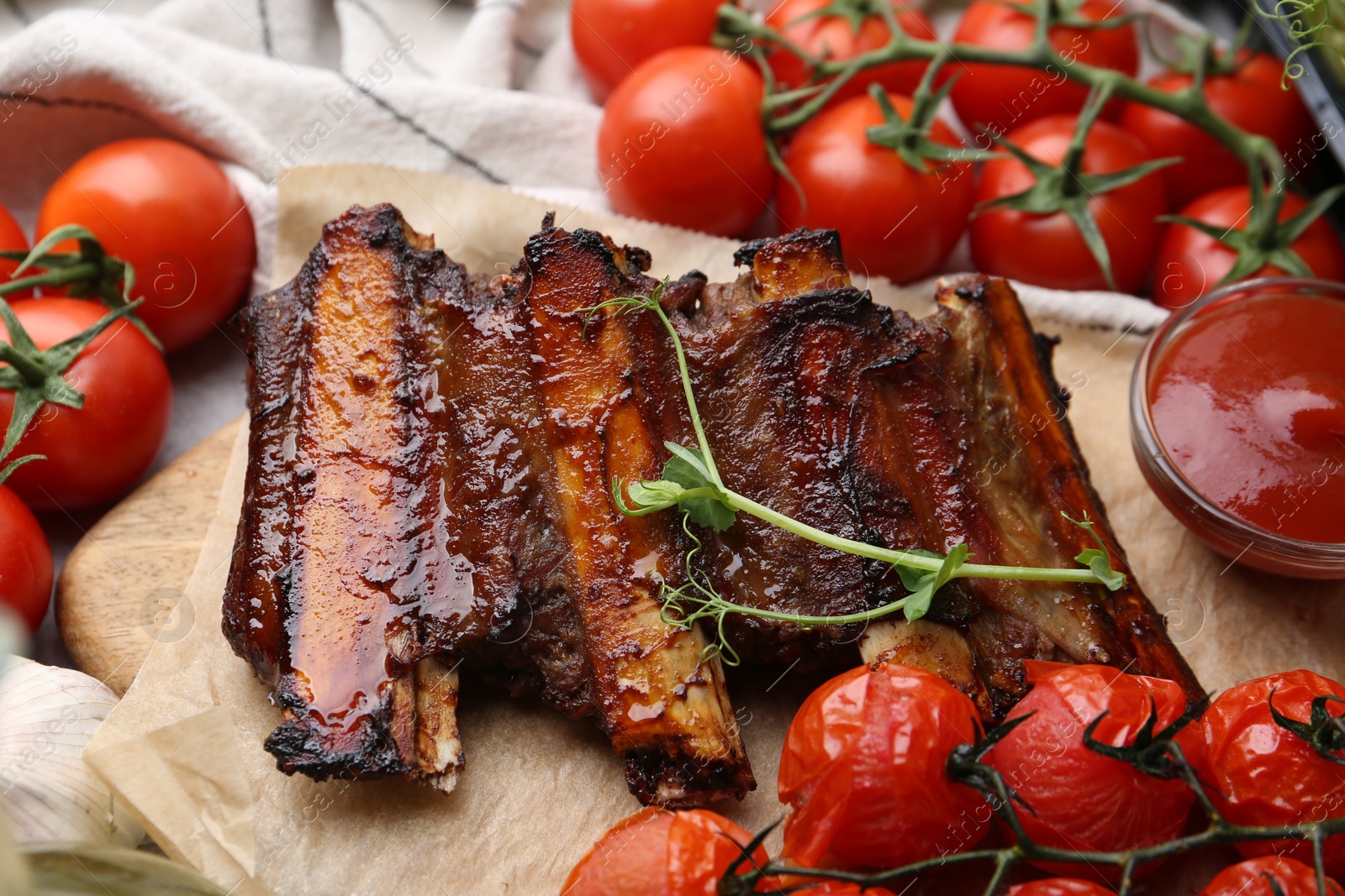 Roasted beef ribs with microgreens, tomatoes and sauce on table, closeup Photo of Roasted beef ribs with microgreens, tomatoes and sauce on table, closeup
