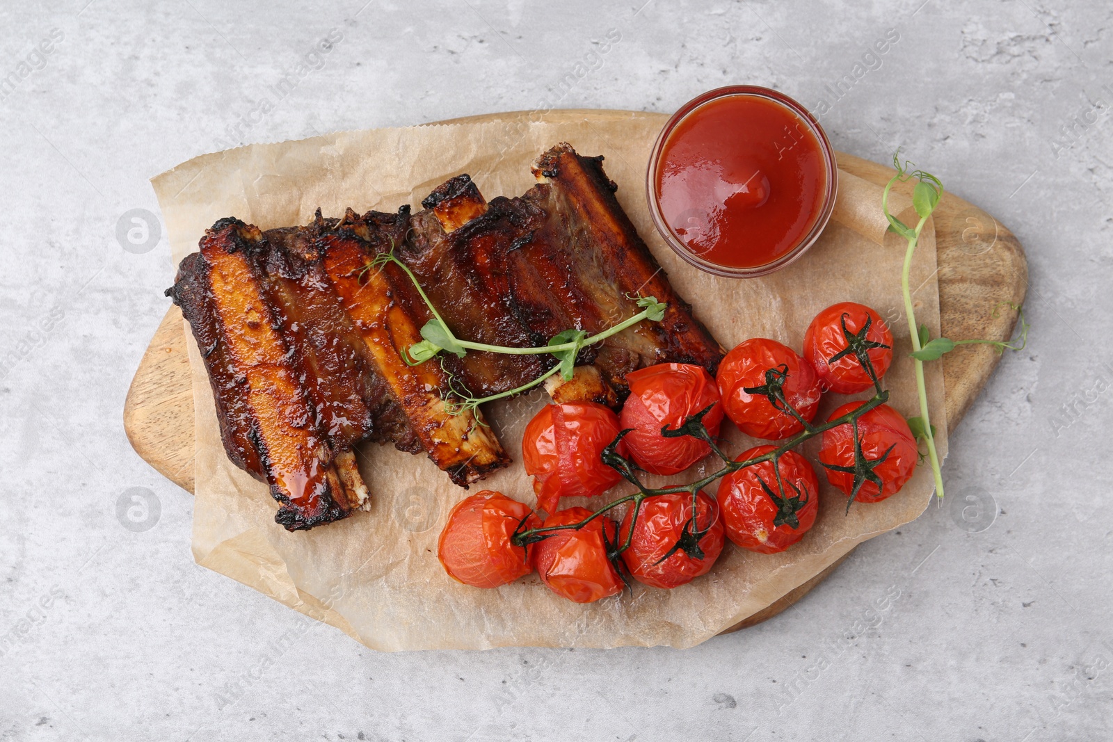 Roasted beef ribs with microgreens, tomatoes and sauce on gray textured table, top view Photo of Roasted beef ribs with microgreens, tomatoes and sauce on gray textured table, top view