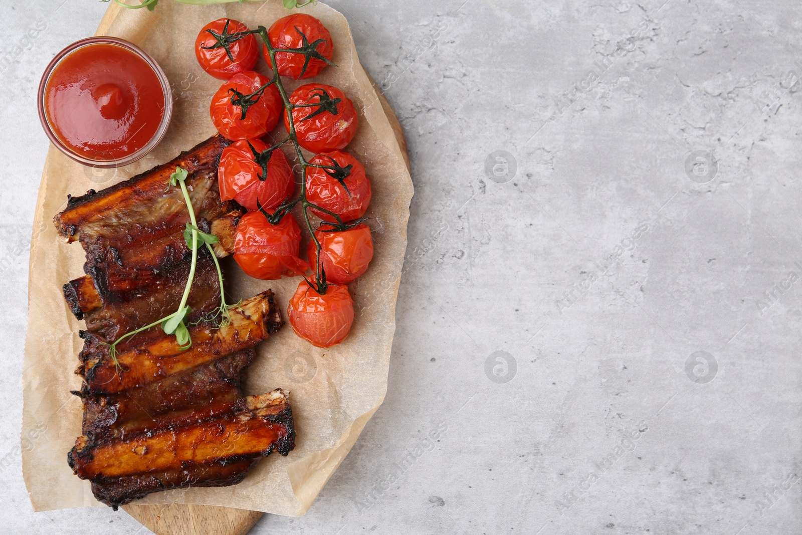 Roasted beef ribs with microgreens, tomatoes and sauce on gray textured table, top view. Space for text Photo of Roasted beef ribs with microgreens, tomatoes and sauce on gray textured table, top view. Space for text