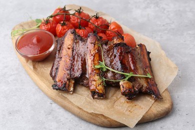 Photo of Roasted beef ribs with microgreens, tomatoes and sauce on gray textured table, closeup