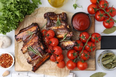 Photo of Roasted beef ribs with rosemary, tomatoes and other products on light table, flat lay
