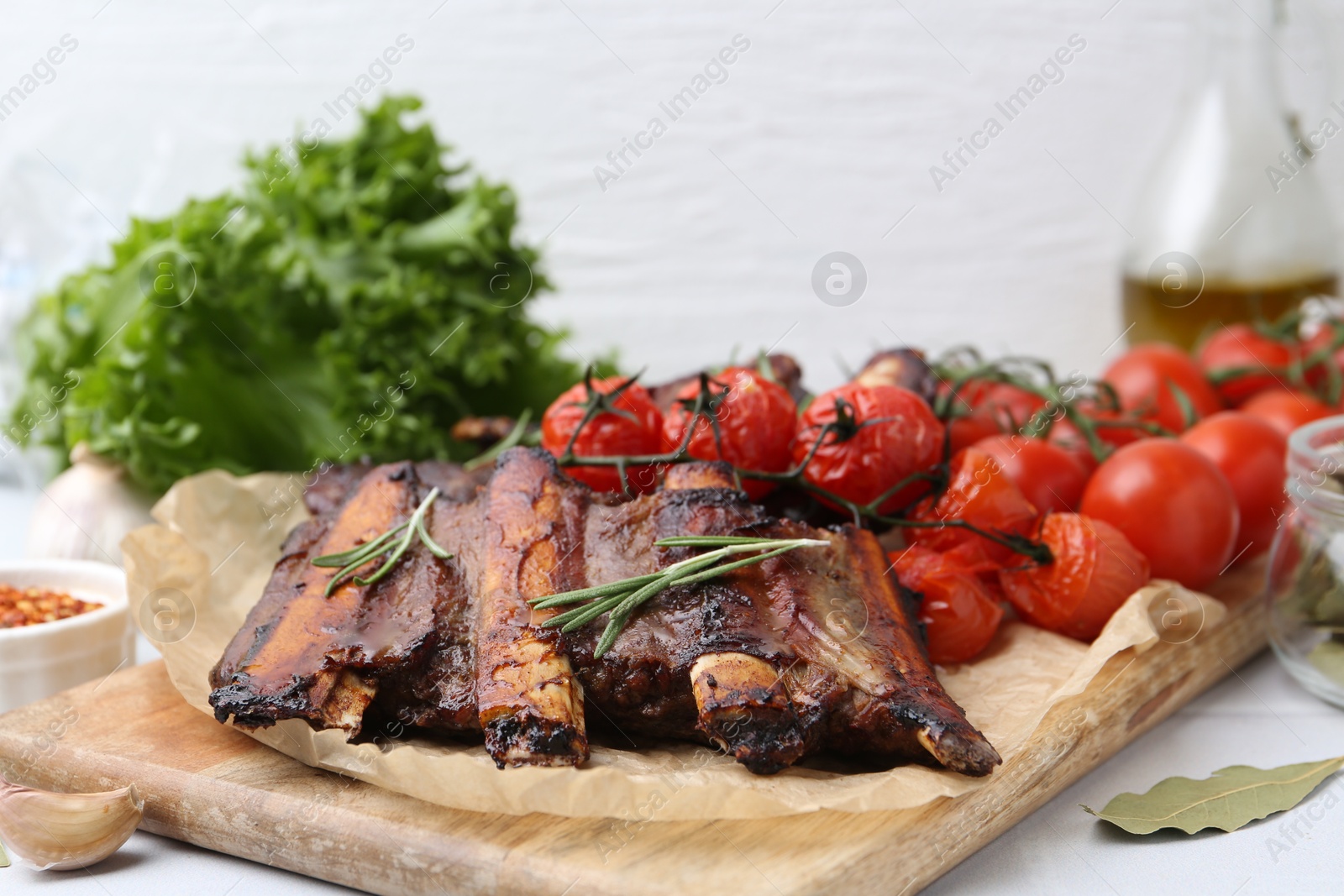 Roasted beef ribs with rosemary, tomatoes and other products on light table, closeup Photo of Roasted beef ribs with rosemary, tomatoes and other products on light table, closeup