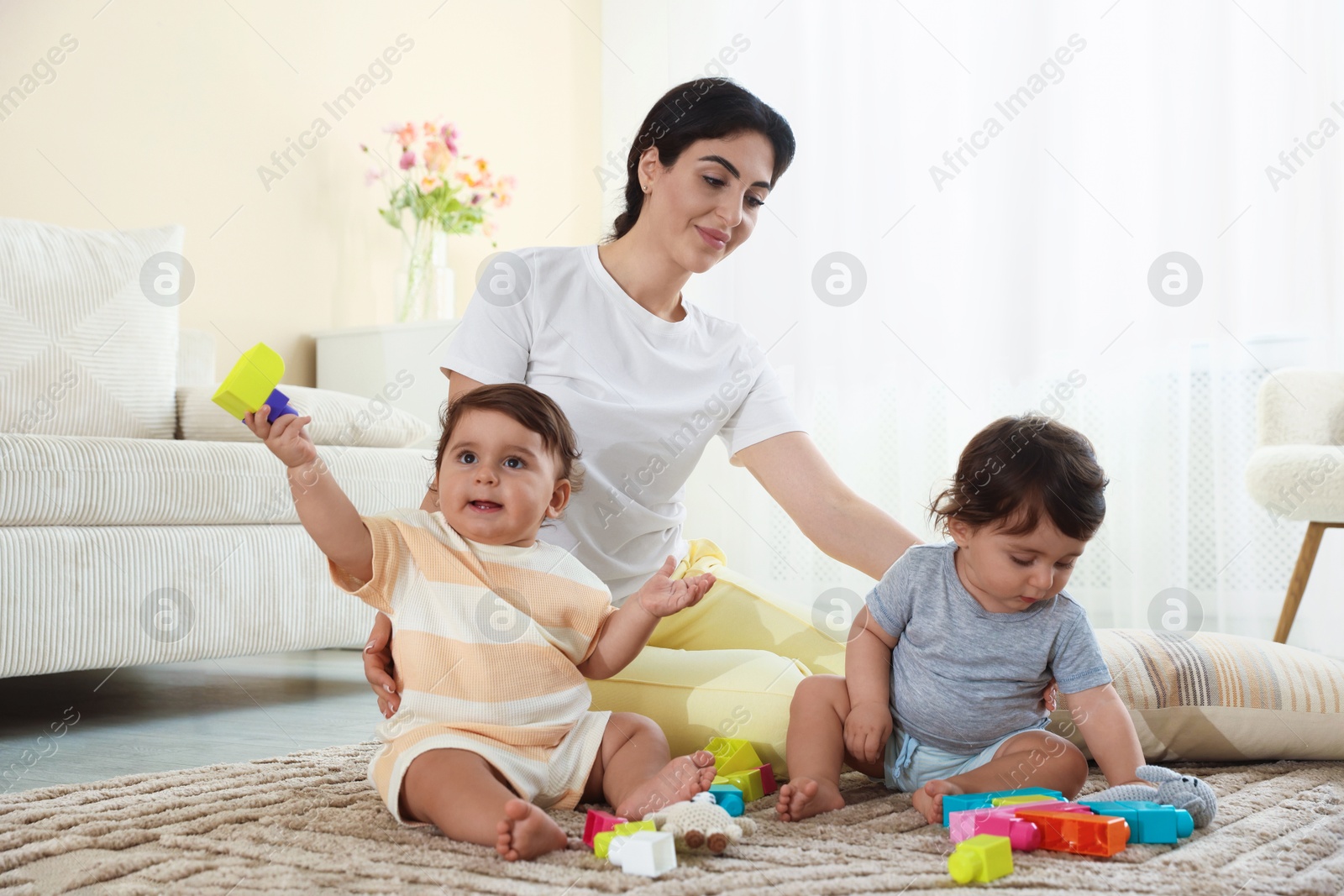 Mother with her cute little twins and toys on floor at home Photo of Mother with her cute little twins and toys on floor at home