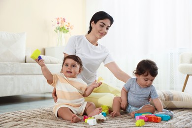 Photo of Mother with her cute little twins and toys on floor at home