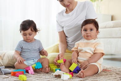 Photo of Mother with her cute little twins and toys on floor at home