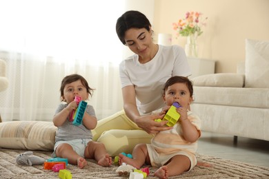Photo of Mother with her cute little twins and toys on floor at home