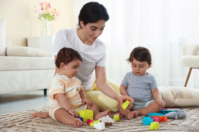 Photo of Mother with her cute little twins and toys on floor at home