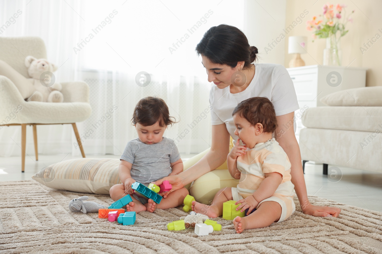 Mother with her cute little twins and toys on floor at home Photo of Mother with her cute little twins and toys on floor at home