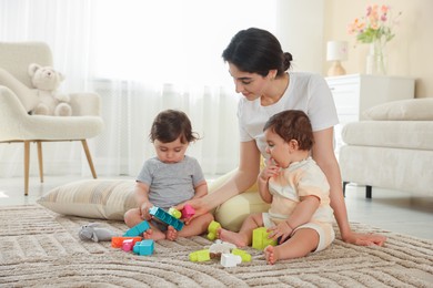 Photo of Mother with her cute little twins and toys on floor at home