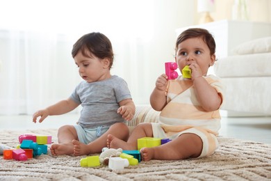 Photo of Cute little twin babies playing with toys on floor at home