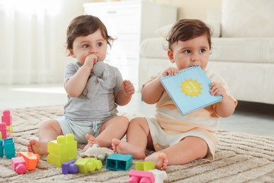 Photo of Cute little twin babies playing with toys on floor at home
