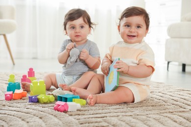 Photo of Cute little twin babies playing with toys on floor at home