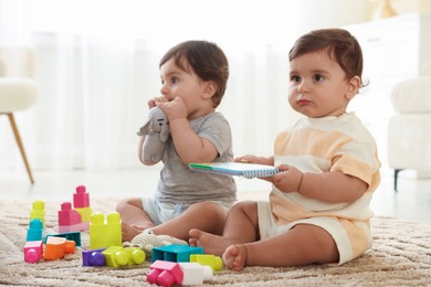 Photo of Cute little twin babies playing with toys on floor at home
