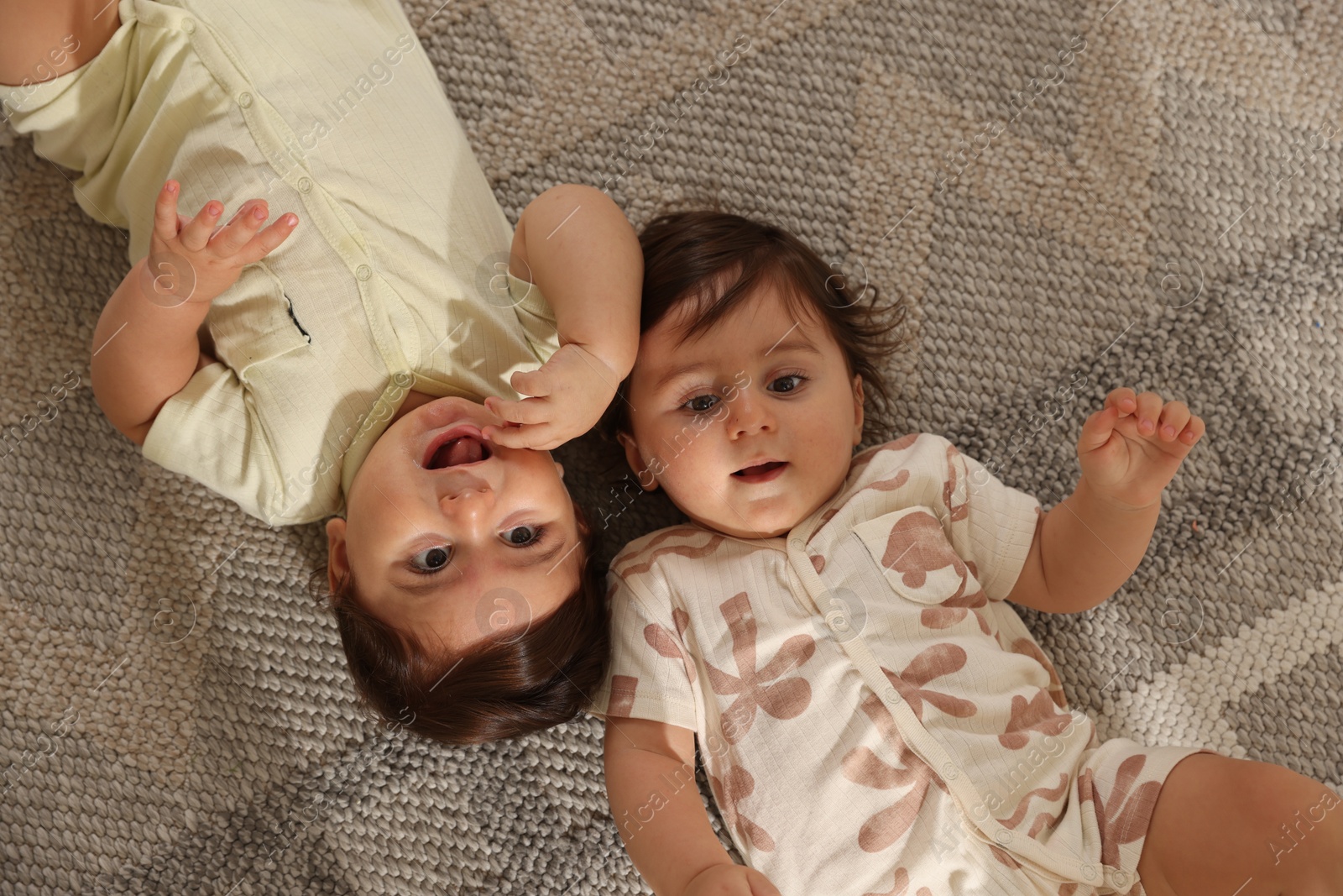 Cute little twin babies on floor at home, above view Photo of Cute little twin babies on floor at home, above view