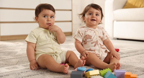 Photo of Cute little twin babies playing with toys on floor at home