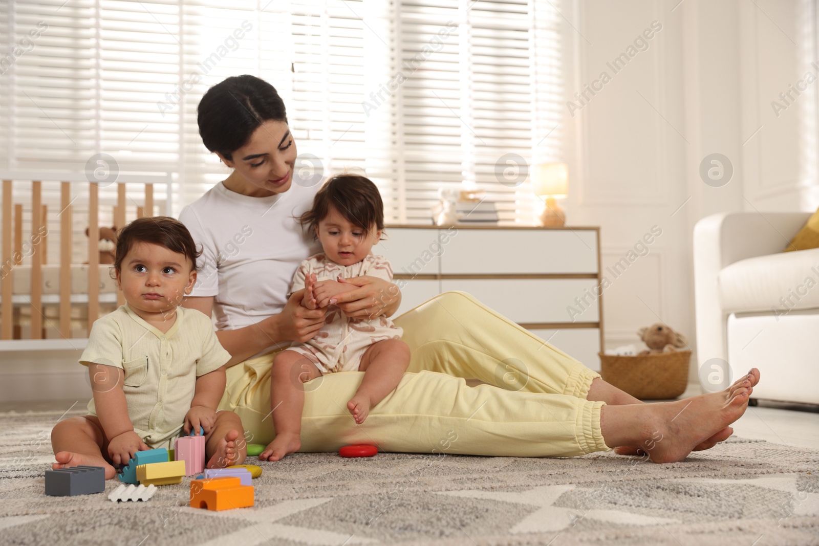 Mother with her cute little twins and toys on floor at home Photo of Mother with her cute little twins and toys on floor at home