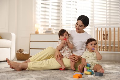 Photo of Mother with her cute little twins and toys on floor at home